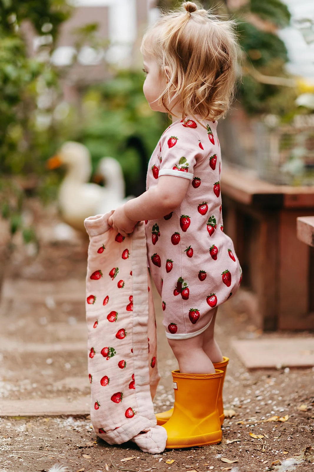 A baby sits smiling while wearing a light blue zipped romper with a bee print.
