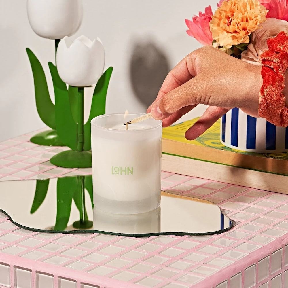 Two candles in aluminum tins with light blue sleeves surrounded by lavender, a cup of tea and a lily.
