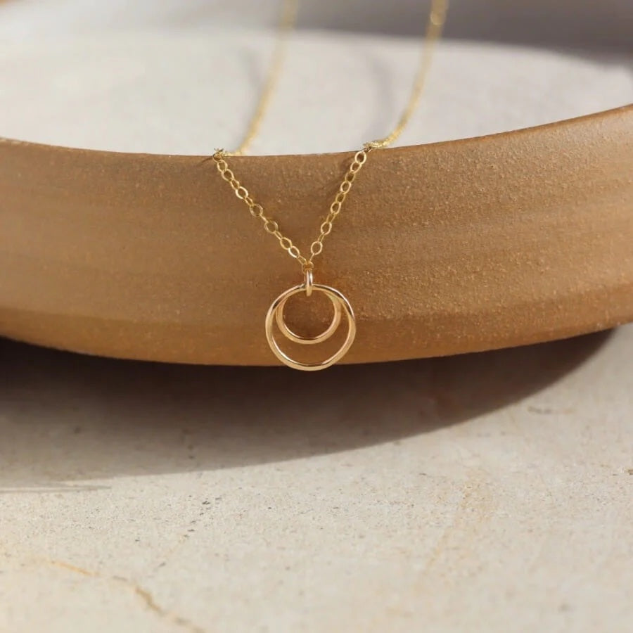 A gold necklace  features two lightly hammered circles suspended on a delicate chain.