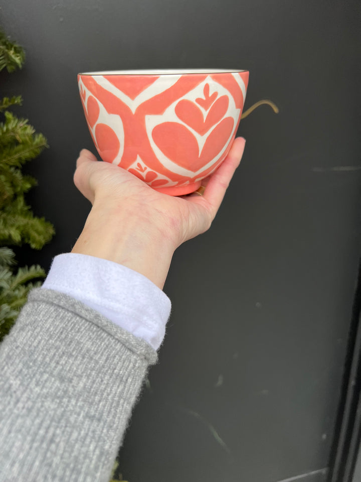 A red/pinkish hand painted bowl with a leafy pattern hand painted on it and a gold rim.