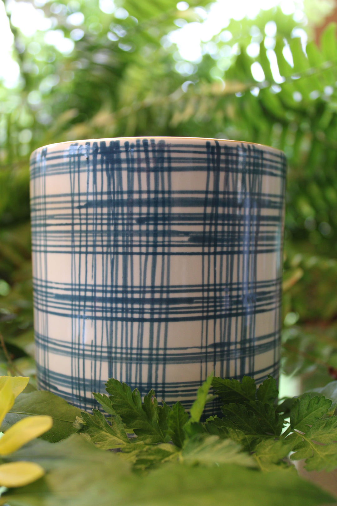 A short wide vase with a hand painted blue pattern on it and a gold rim.