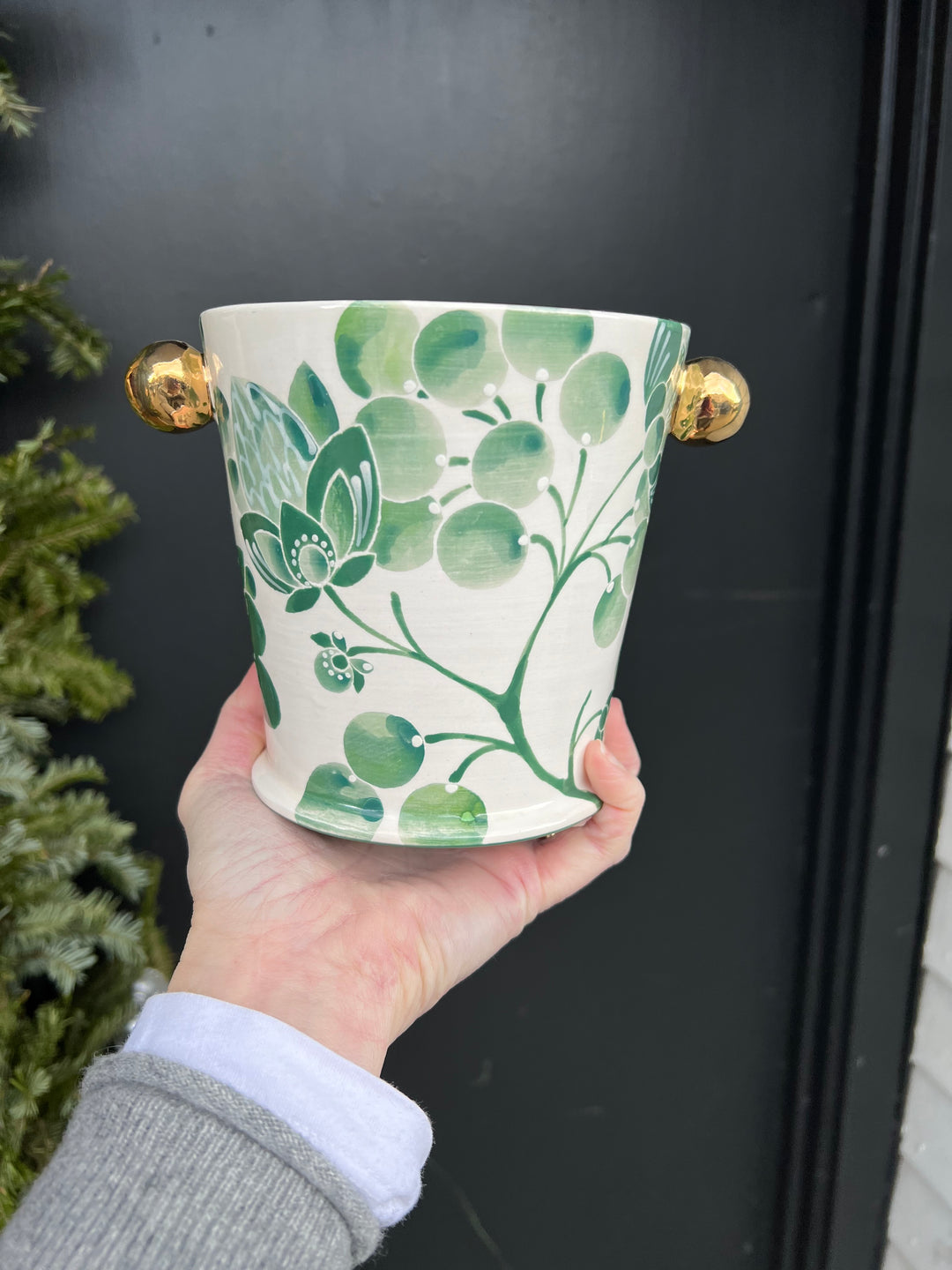 A small herb pot hand painted with a green floral pattern and gold knobs and rim.