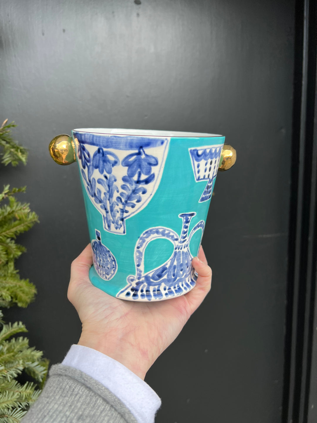 A small turquoise herb pot hand painted with a blue and white china pattern and gold knobs and rim.