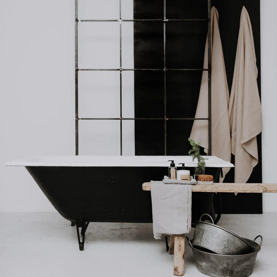 A black cast iron free standing bath tub with a glass bottle of lotion next to it.