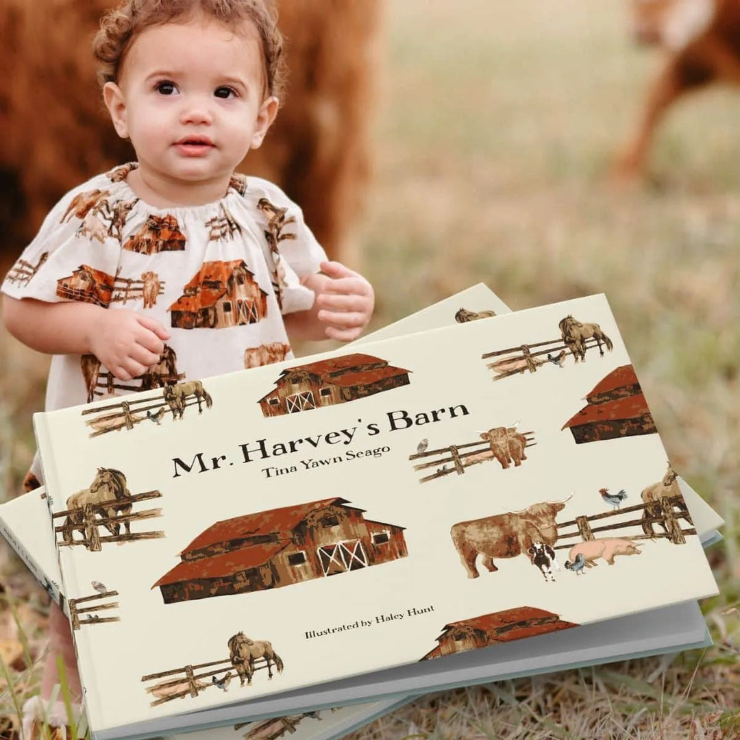 A child in a barn yard sits near a book entitles "Mr. Harvey's Barn"