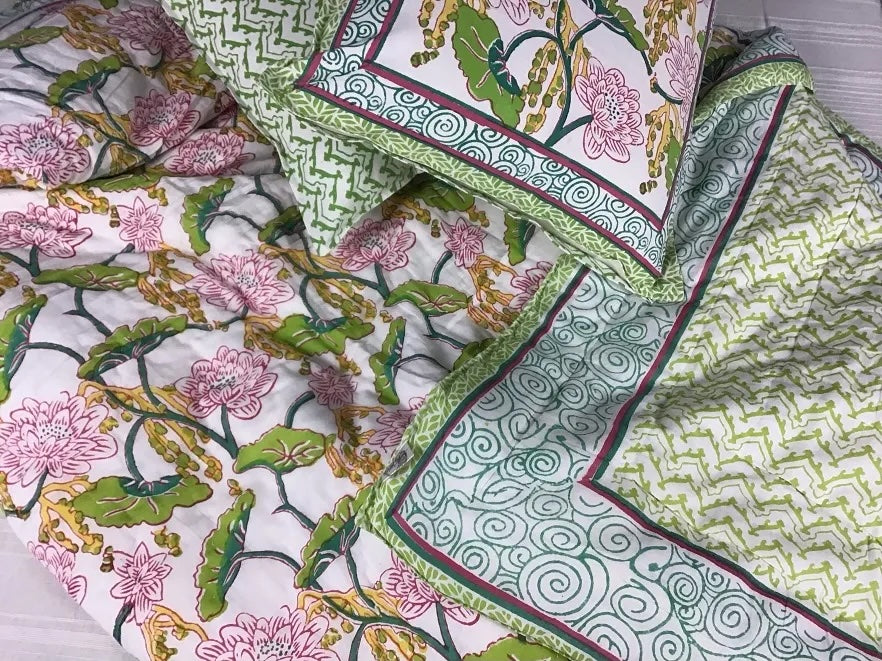 A colorful quilt and matching pillow cases with a pink floral and green leaf designs.