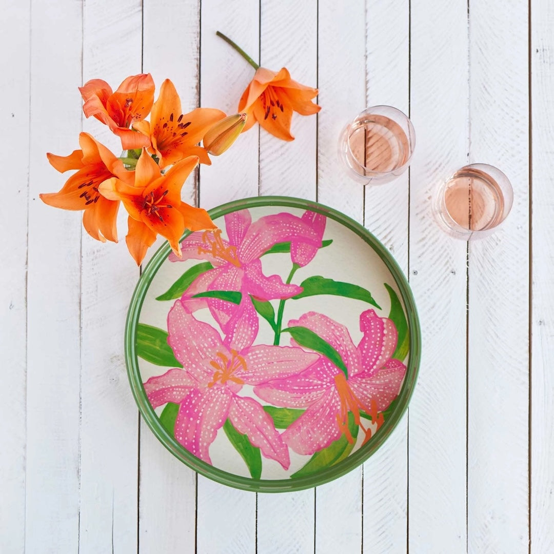 A round kitchen tray with green edges and large bright pink lilies printed on it.