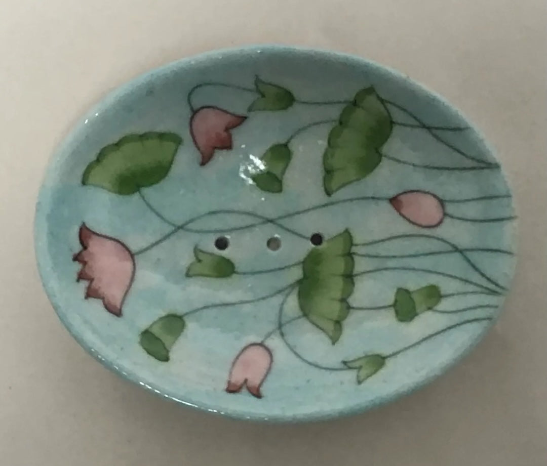 A ceramic soap dish with pink and green flowers on a light blue background.
