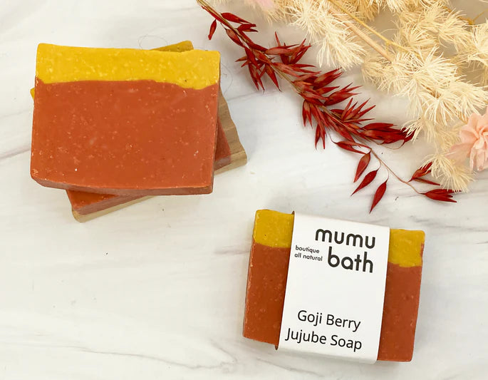 Colorful Brick red and dark yellow soap (Goji Berry Jujube Soap) sit amongst dried foliage of similar colors.