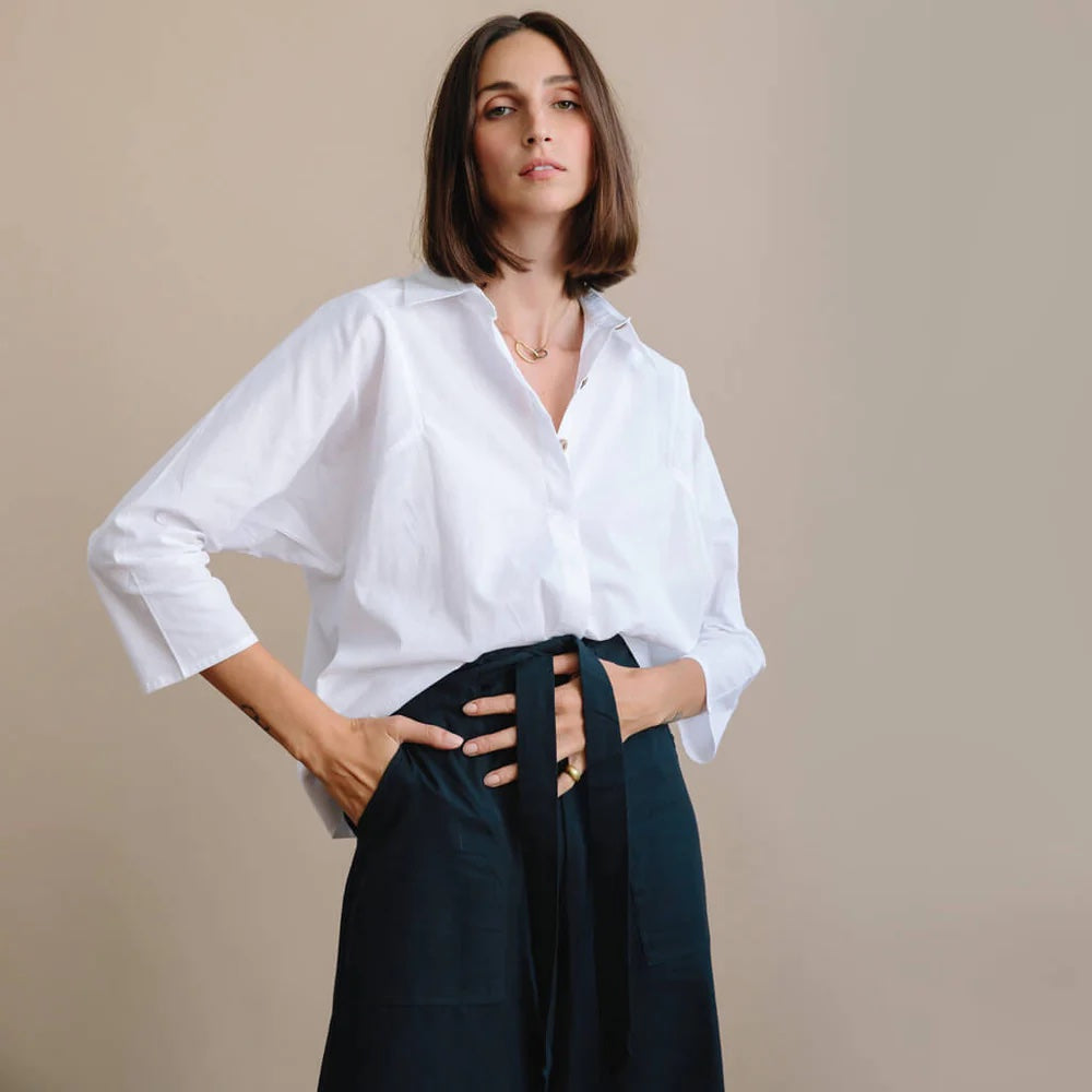 A white lady wears a white button-down and wide leg black pants with a bow tie at the waist.