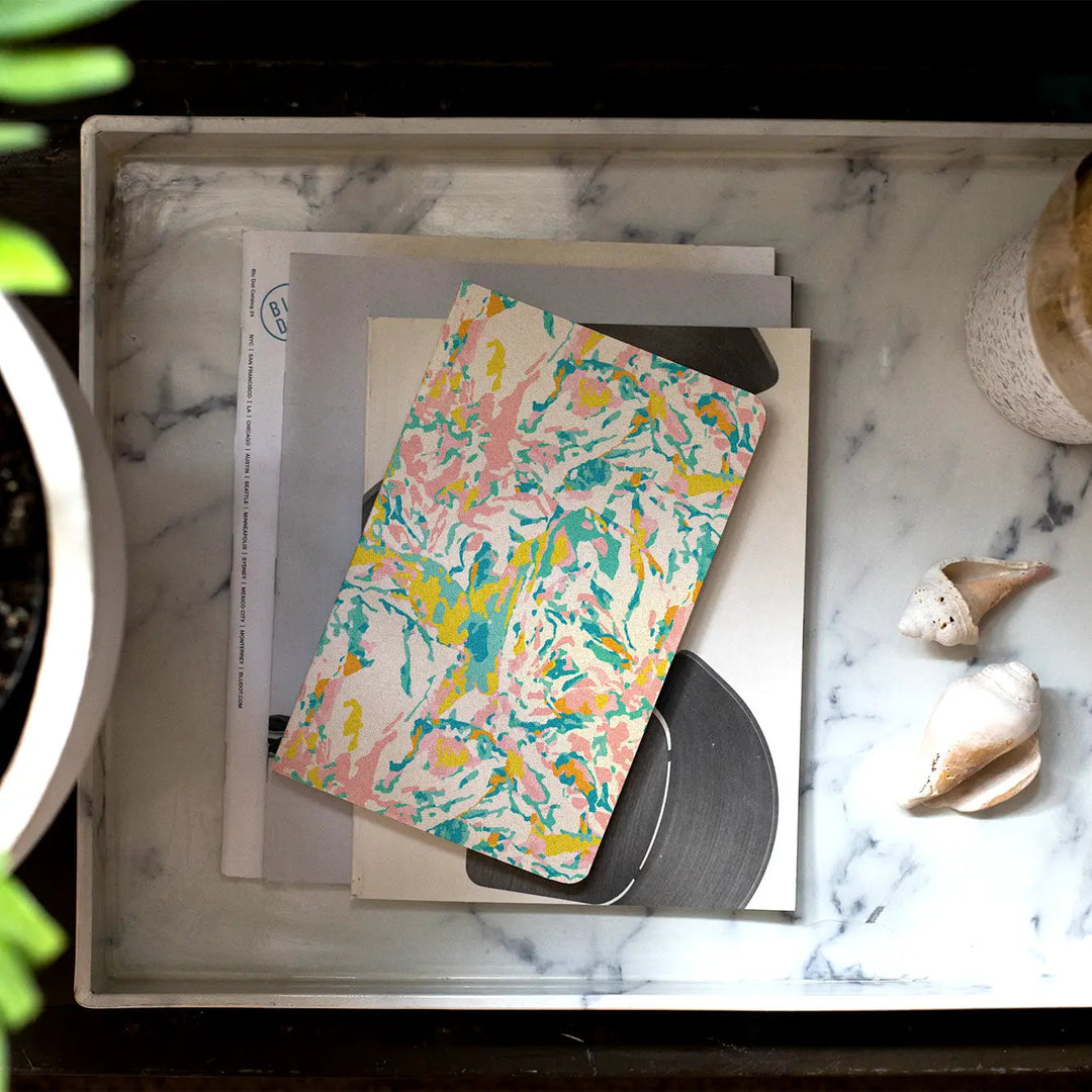 A marble colored notebook with pinks, greens and yellows sits on a desk.