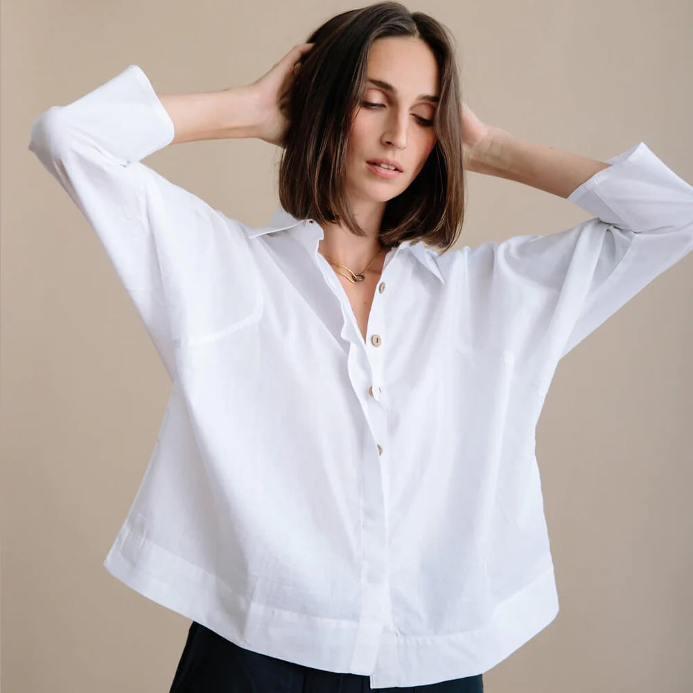 A lady holds her hands up, showing off a white cotton button down boxy shirt.