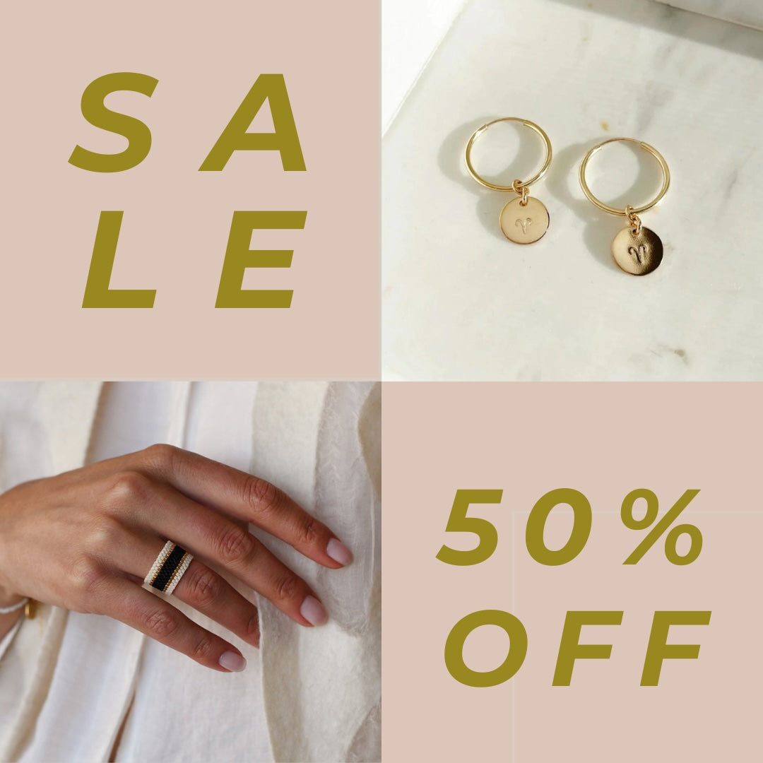 A sign reads "Sale" and "50% Off" and pictures gold colored drop earrings and a beaded banded ring.