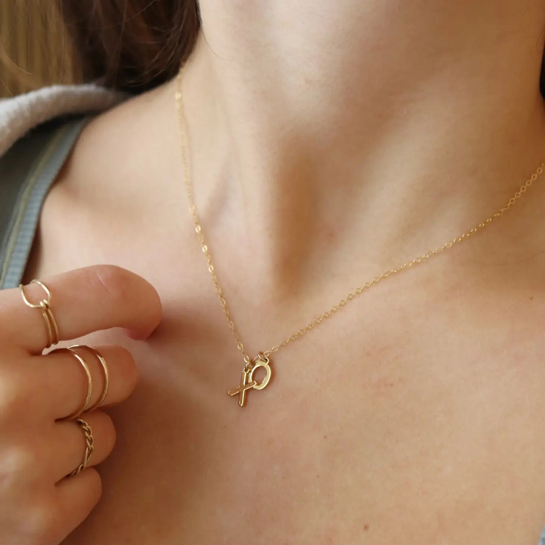 A lady's neck wears a gold colored necklace with a simple chain and small "x" and "o" letters attached to the chain.