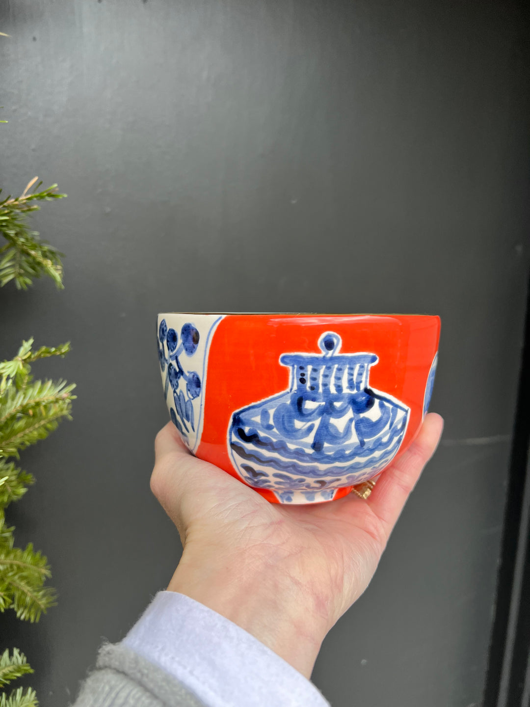 A dark red/orange hand painted bowl with white and blue painted china patterns on it and a gold rim.