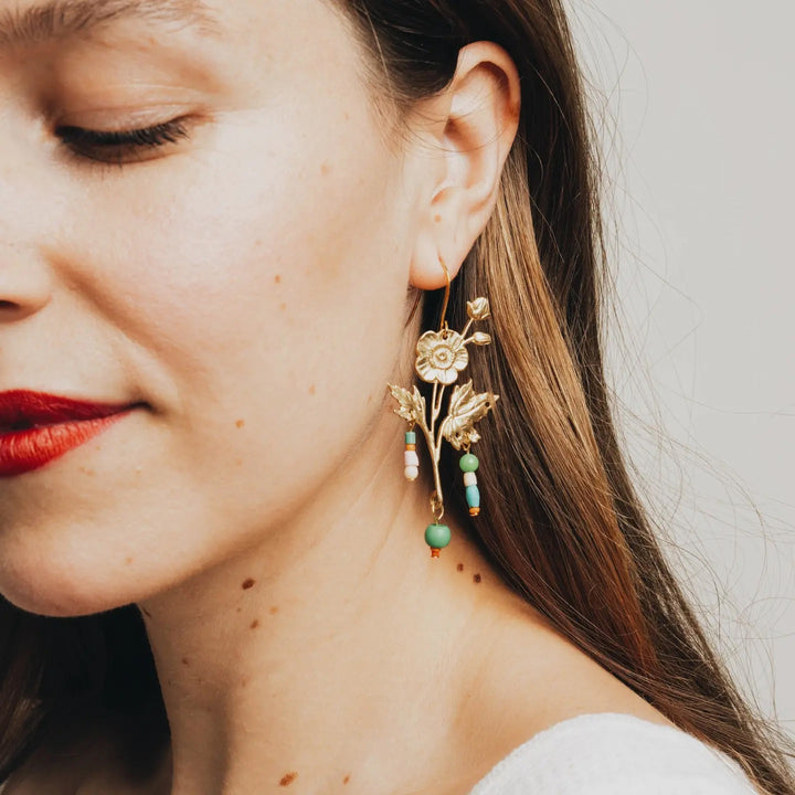 A lady wearing floral shaped gold colored earrings with colorful beads dangling.